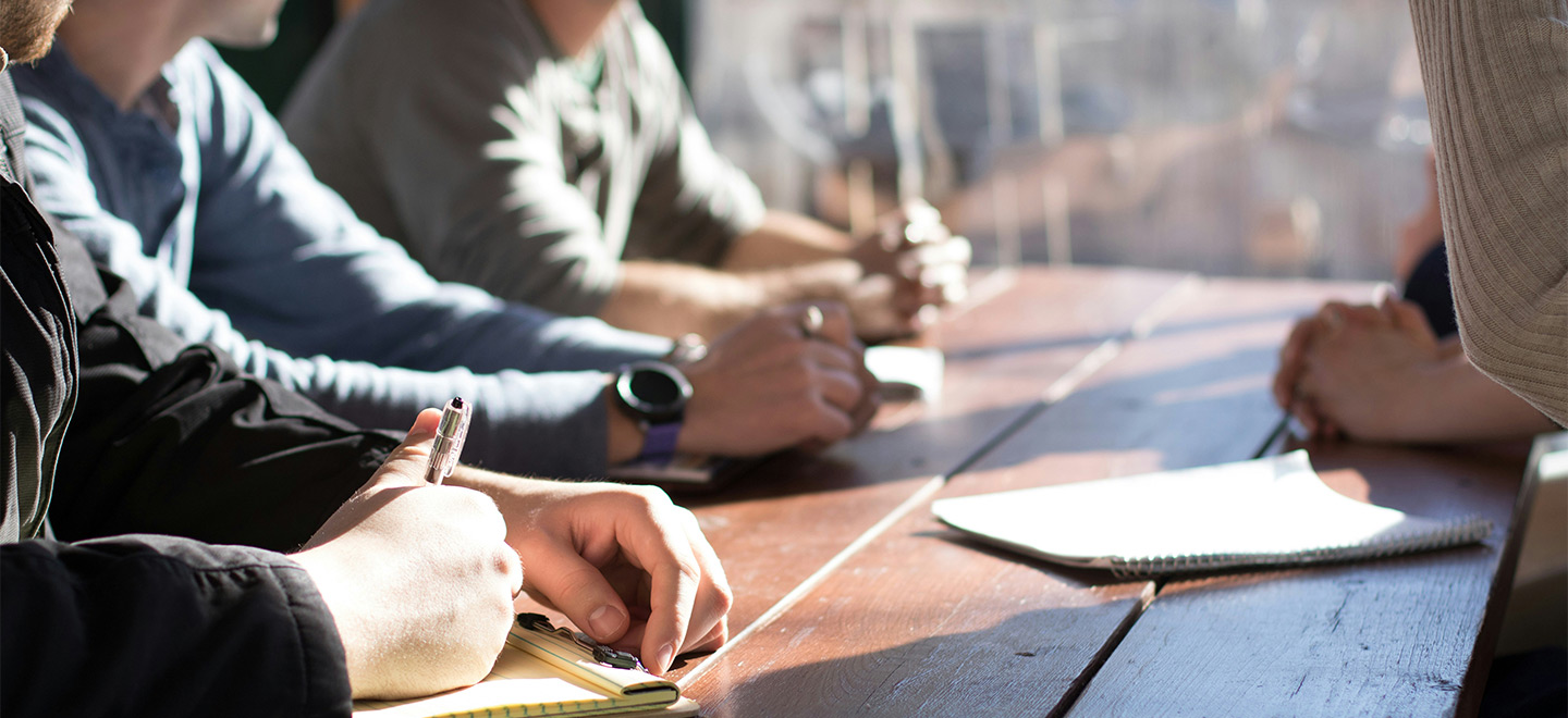 Menschen sitzen an einem Tisch mit Notizblöcken vor sich